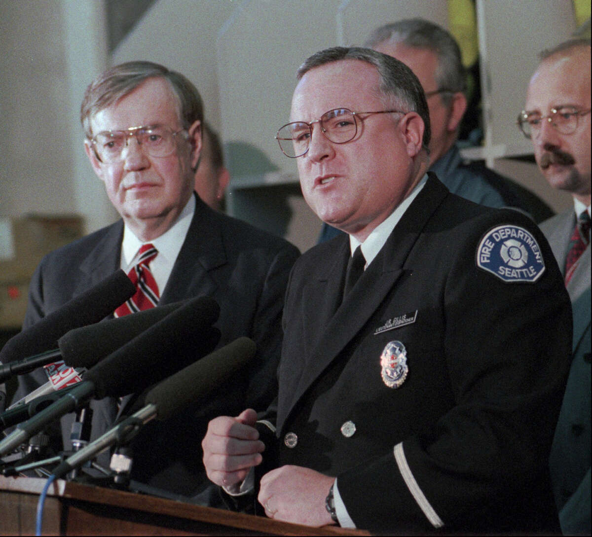 Seattle Fireman J. R. Gillis, at microphone, makes his feelings known Tuesday, Jan. 2, 1995 about the return of Martin Pang from Brazil to Seattle to face charges in a warehouse fire that killed four firemen. Behind Gillis is King County Prosecutor Norm Maleng. Pang fled to Brazil after the fire. (AP Photo/Barry Sweet)