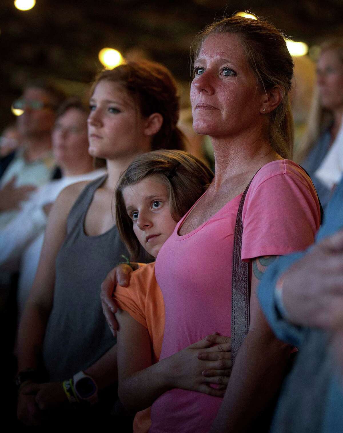 A woman stands with her family as a prayer is said over the loudspeakers at the Prescott Frontier Days Rodeo, Wednesday, July 3, 2013 in Prescott, Ariz., for the 19 Granite Mountain Hotshot firefighters who were killed Sunday near Yarnell, Ariz. (AP Photo/Julie Jacobson)