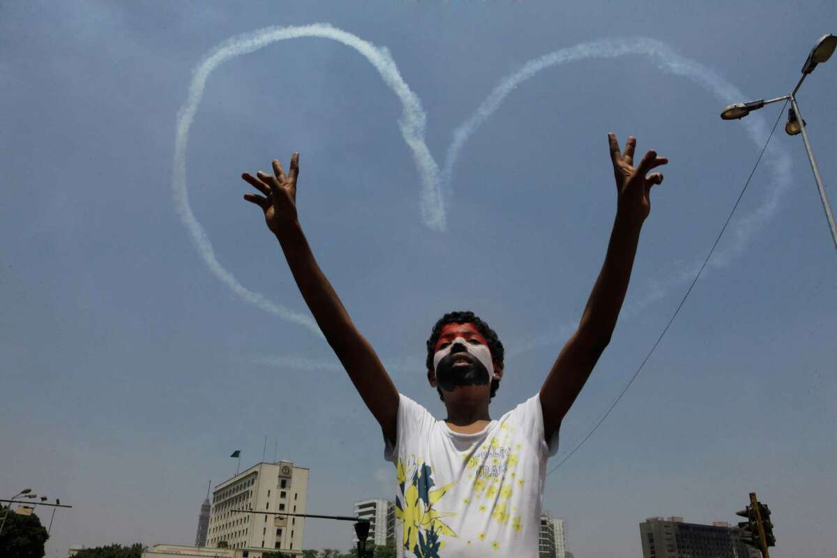 An Egyptian protester flashes v signs for military aircrafts forming a heart shape trails in the sky Friday over Tahrir Square in Cairo, Egypt. Egypt's Muslim Brotherhood called for a wave of protests Friday, furious over the military's ouster of its president and arrest of its revered leader and other top figures, underlining the touchy issue of what role the fundamentalist Islamist movement might play in the new regime. (AP Photo/Amr Nabil)
