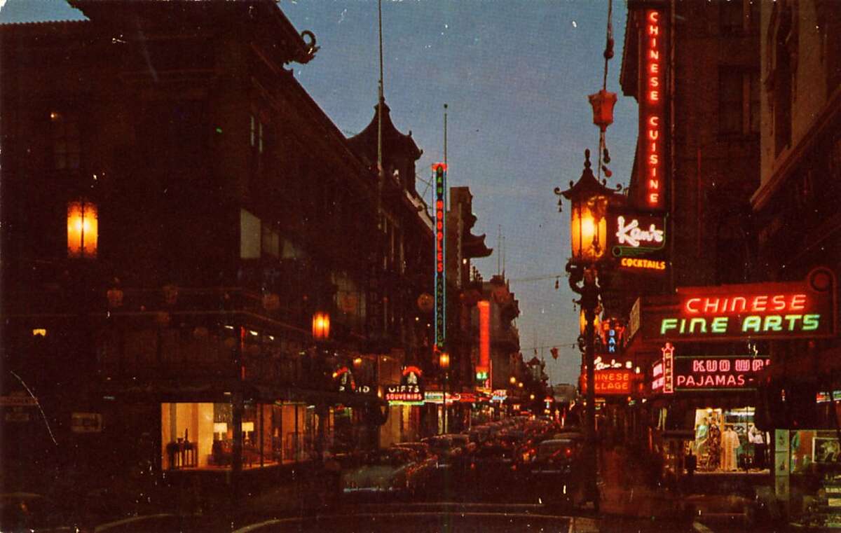 A night view of San Francisco's Chinatown in the 1950's. The streets are crowded with traffic and neon signs light up the night.