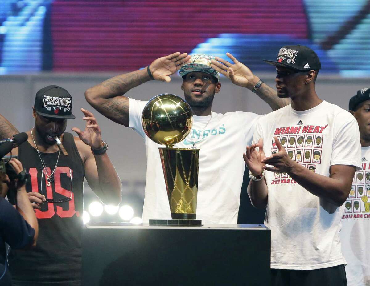 Miami Heat small forward LeBron James, center, salutes the crowd after touching the Larry O'Brien NBA Championship Trophy as shooting guard Dwyane Wade, left, and center Chris Bosh, right, look on, Monday, June 24, 2013 during a celebration for season ticket holders at the American Airlines Arena in Miami. The Heat defeated the San Antonio Spurs 95-88 in Game 7 to win their second straight NBA championship. (AP Photo/Wilfredo Lee)