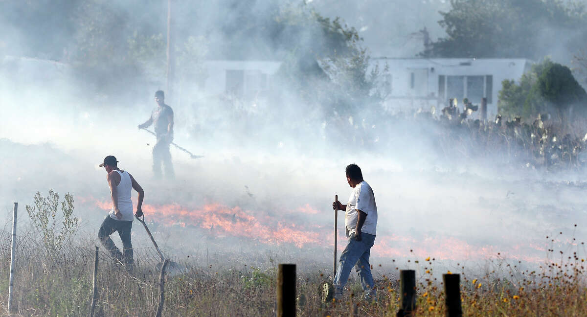 Residents use shovels to fight a grass fire off IH-35 South Monday Aug. 5, 2013 near Natalia, Tx.