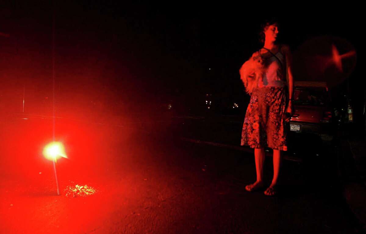 A woman holds her dog whilst she stands next to a flare during a massive blackout August 15, 2003 in New York City. Power is slowly returning to certain parts of the city.