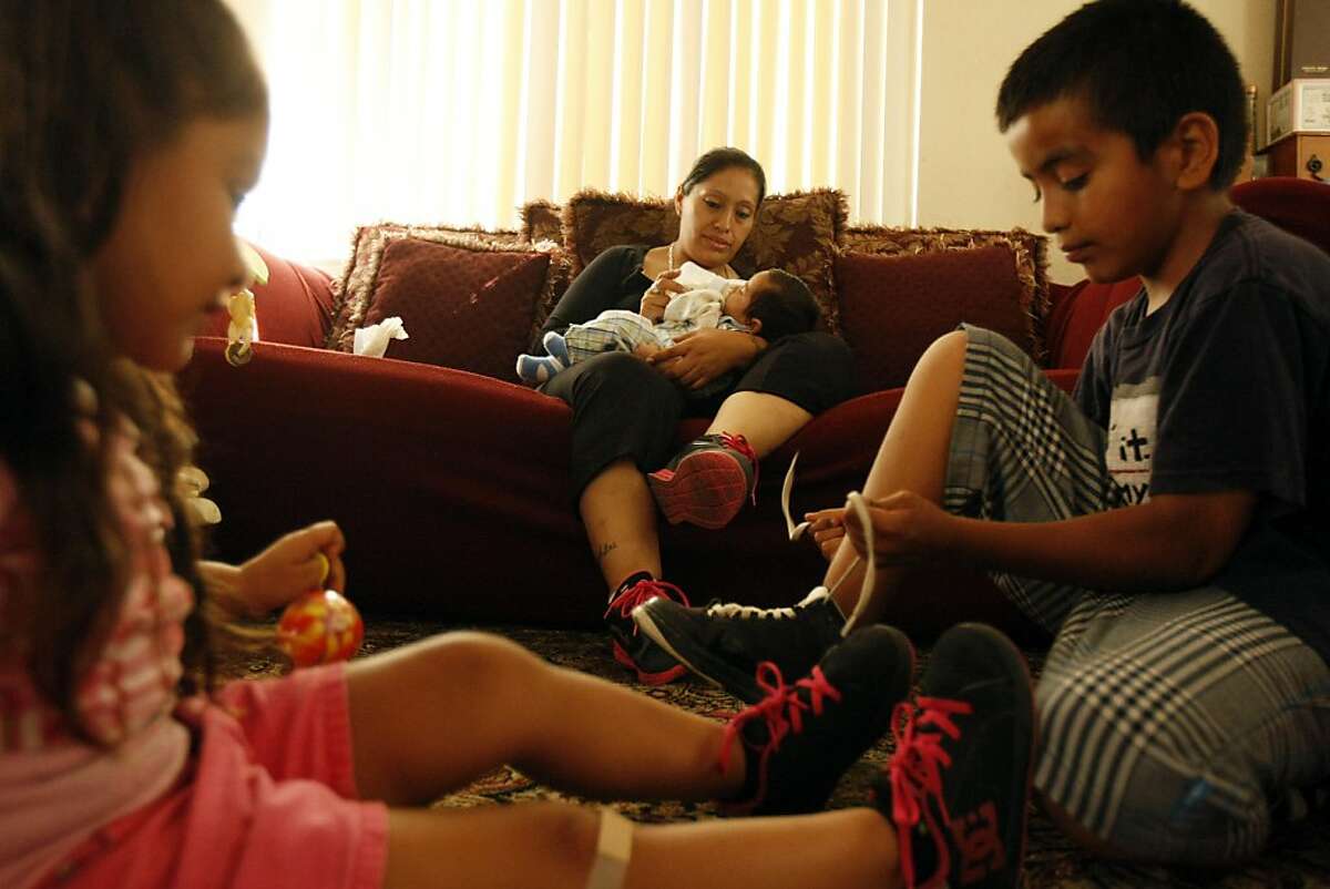 Maria Lorena Pulido feeds her youngest son Joseph while Angel shows Nephertytie how to tie her shoelaces on Thursday, 08 August, 2013, in Menlo Park, Calif.