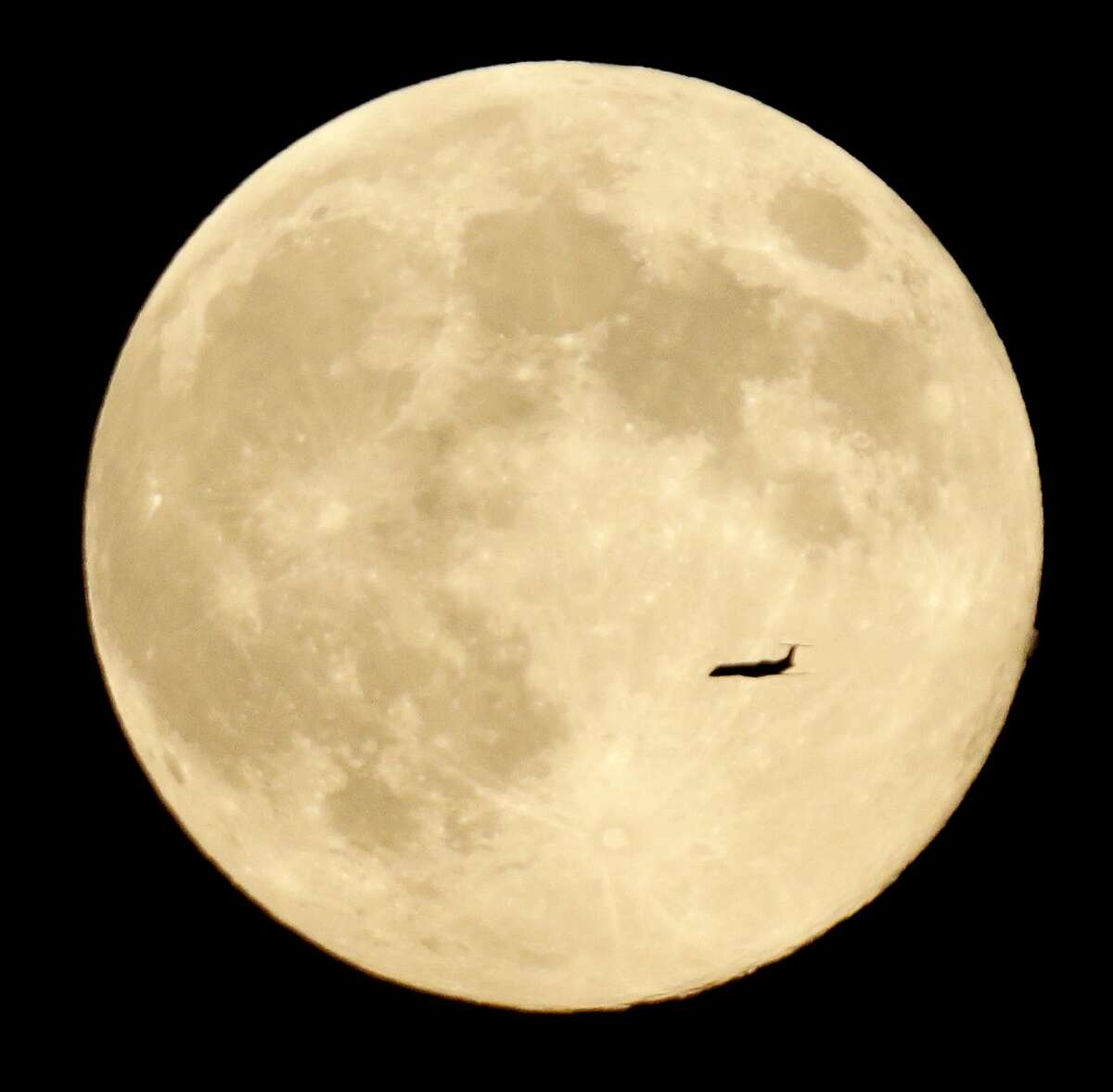 A plane cruises in front of the moon in its full stage under a phenomenon called the blue moon, as seen from West Orange, N.J., Tuesday, Aug. 20, 2013. (AP Photo/Julio Cortez)
