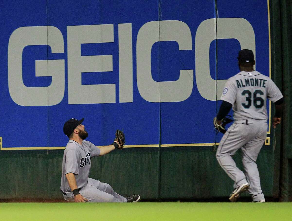 Seattle center fielder Dustin Ackley (13) slides into the bottom of the outfield wall as he catches a fly ball hit by the Astros' Robbie Grossman in the fifth inning.