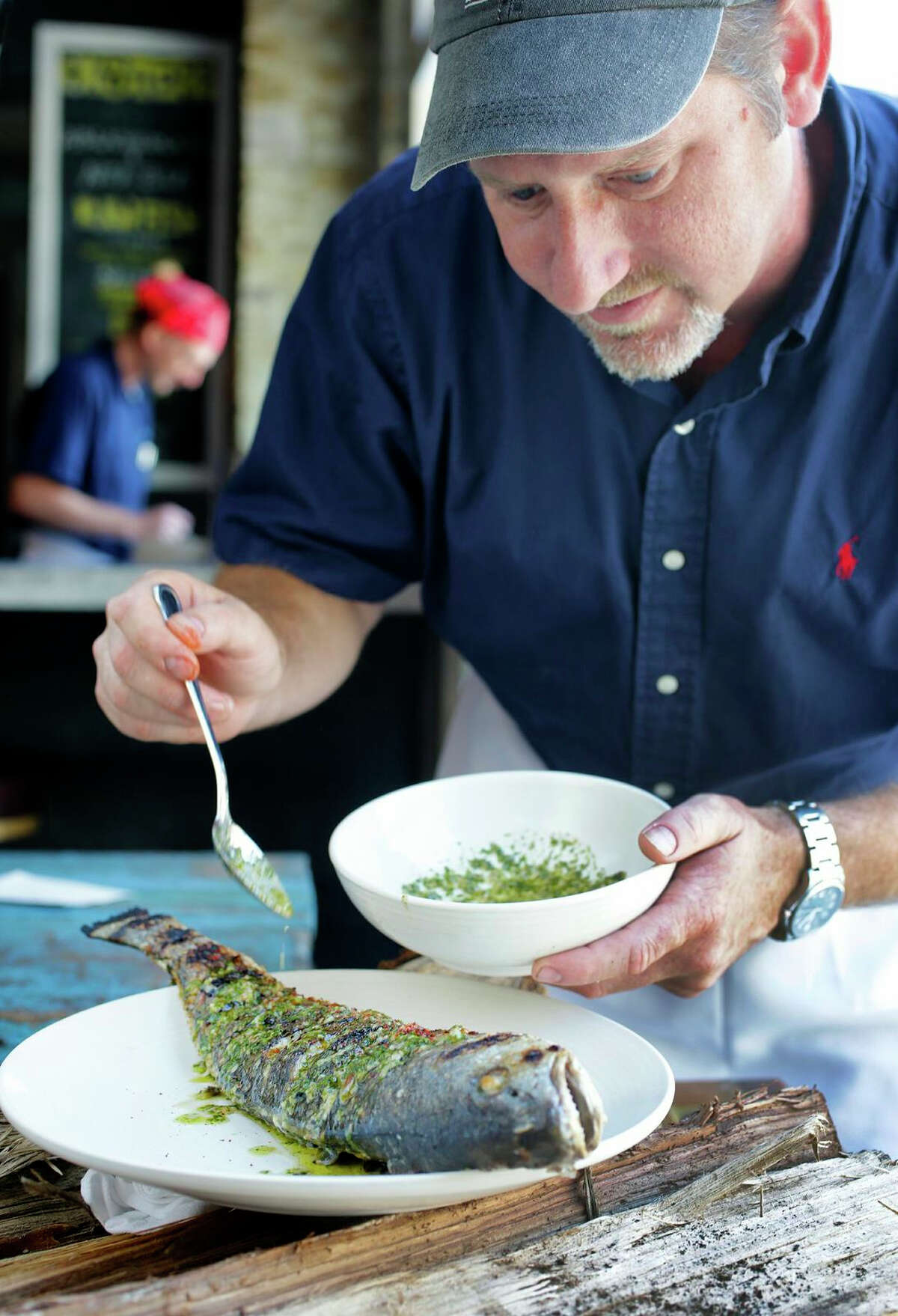 Donald Link, chef and co-owner of Peche Seafood Grill ladles a green sauce (fresh mint, parsley, lemon, garlic and olive oil, plus dried flakes of the sweet, slightly hot Crilloa sella chiles) over whole grilled fish.