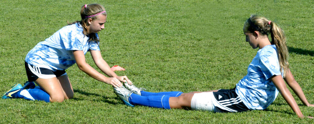 The Spartans' Sarah Stratton helps teammate Caroline Kelly stretch out prior to a pre-season scrimmage for Shepaug Valley High School girls' soccer. September 2013