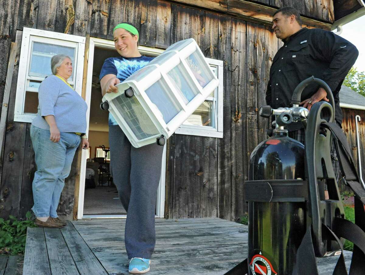 Cohoes High School student Emily Taylor, 16, carries plastic drawers out of a room that needs it's carpet replaced at Brian Holloway's Stephentown, N.Y. house on Tuesday, Sept. 17, 2013. One of the student's mother SandiLyn Rivet, left, who was also there to help talks to Brian Holloway. (Lori Van Buren / Times Union)