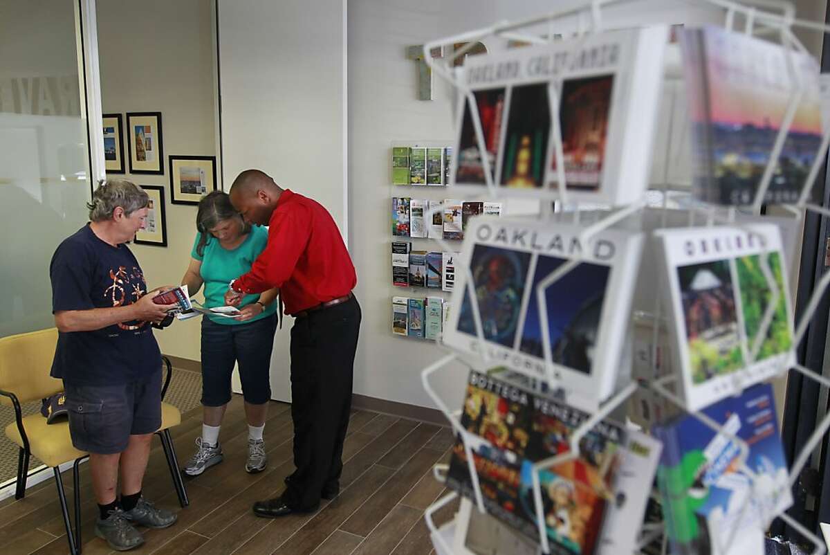 Visitor center coordinator Bostyon Johnson, (right) shares information with Oakland residents Gilles and Martha Bureau, at the Visit Oakland Center, on Tuesday Sept. 17, 2013, at Jack London Square in Oakland, Calif. They will share the information with friends who will be visiting from France. The City of Oakland is renewing it's push to convince tourists that the city is safe by opening a visitors center designed to encourage people to visit.