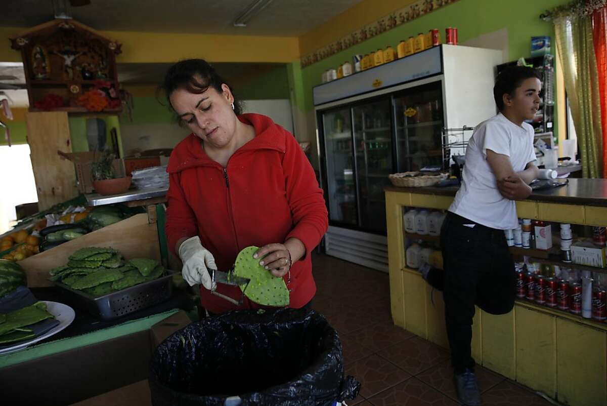 Emelia Gonzalez (l to r) removes Nopales spines from the pads at her store, Lupita's Produce, as her son Richard Luna, 14, stands at the counter on Wednesday, July 17, 2013 in Salinas, Calif.
