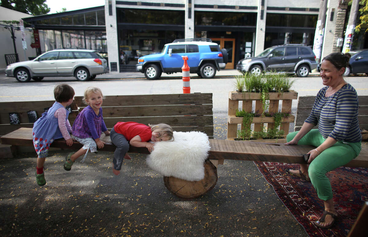 Carrie Barnes, right, rides on a teeter totter with kiddos at the Light Table Design Collective pop-up park on Ballard Avenue NW during PARK(ing) Day on Friday, Sept. 20, 2013. PARK(ing) Day is an event where businesses, community groups and individuals turn parking spaces into pop-up mini parks. There were about 40 of the parks across Seattle.