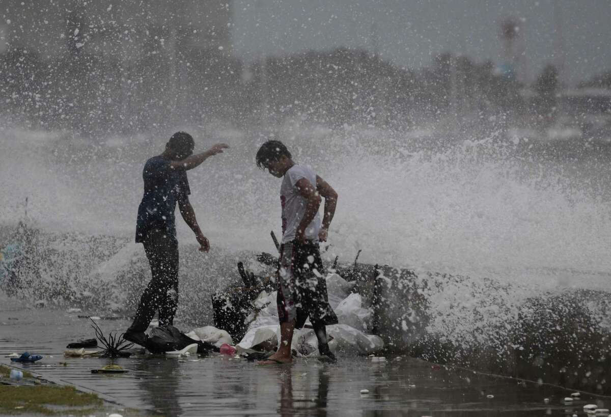 Filipino workers are hit by splashes from a strong wave driven by Typhoon Usagi as it strikes the wall along a bayside promenade in Manila.