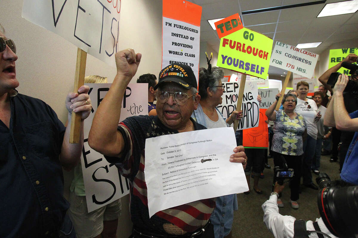 Raul Sanchez (center) raises his arm and holds what protesters called " a notice of immediate furlough" for U.S. Senator Ted Cruz during a demonstration Thursday October 3, 2013 at Cruz's office at Port San Antonio. Federal workers, union members and others gathered in front of and inside of a building there that houses Cruz's office to express their disapproval of Cruz and the recent government shutdown.