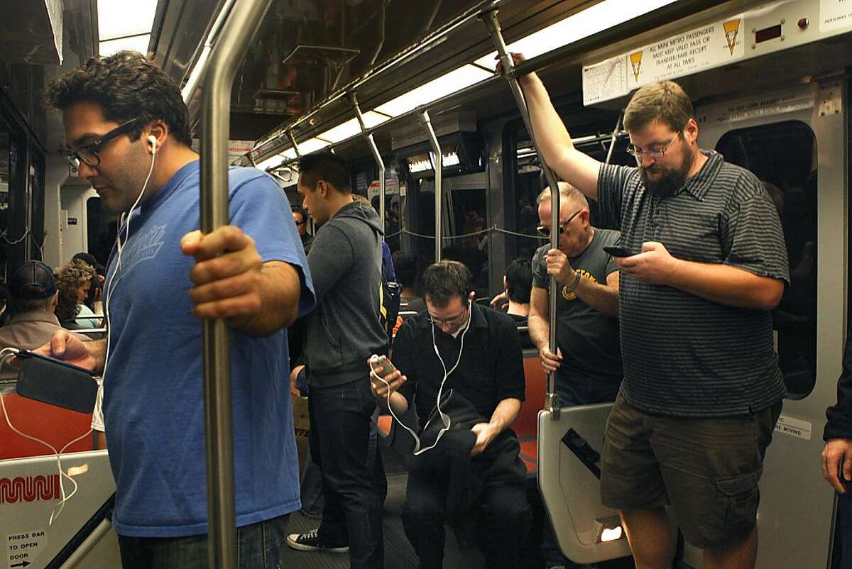 Passengers including Brandon Long (right) on his cell phone while going to work on a Muni train stopping at Powell Street station in San Francisco, California, on Friday, October 4, 2013.