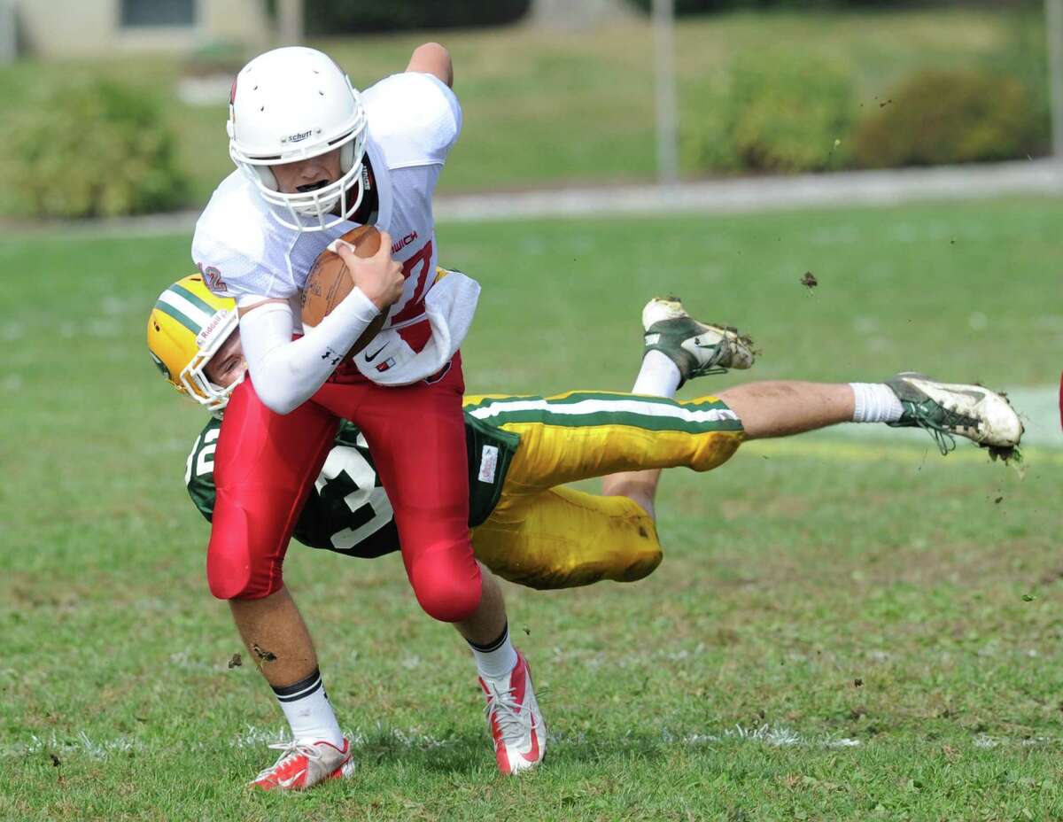 Greenwich quarterback Matt Marzulla, foreground, evades the tackle of Thomas Costigan (# 32) of Trinity Catholic during the high school football game between Greenwich High School and Trinity Catholic High School at Trinity in Stamford, Saturday, Oct. 5, 2013. Greenwich won the game over Trinity Catholic, 42-14.