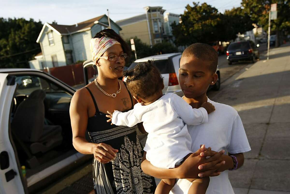 Carjuan Thomas, 13, holds his baby sister Zion Bradford while their mom Dameka Bradford looks on as they visit with friends in front of Upperkutz barber shop in West Oakland, California Wednesday October 2, 2013.