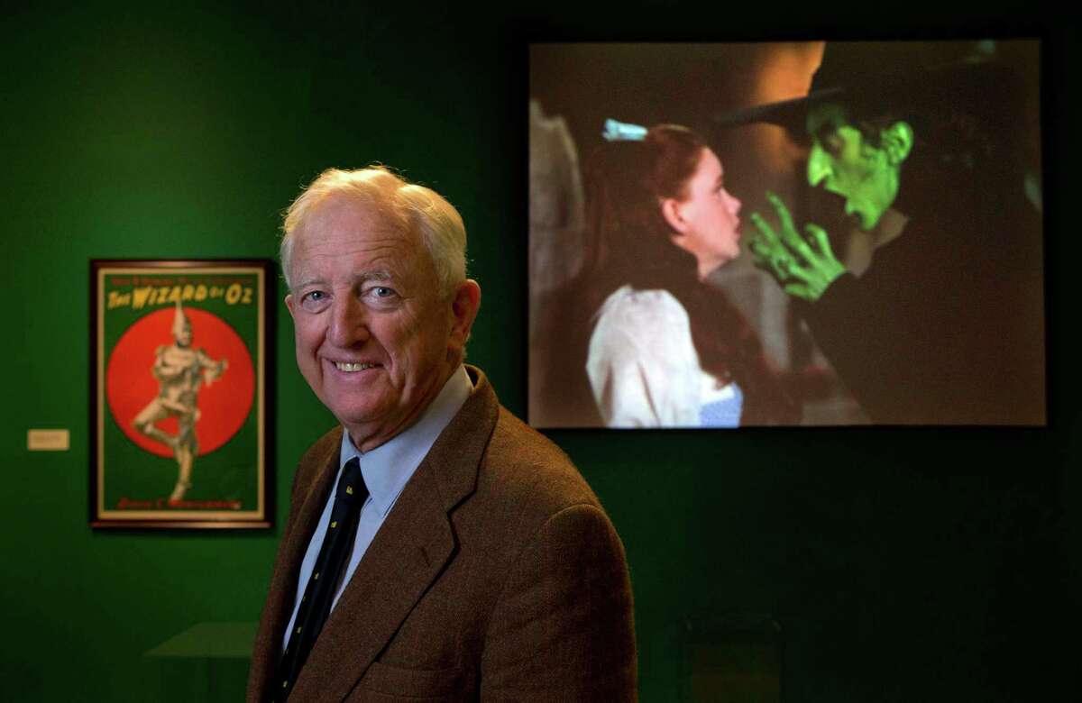 In this Tuesday, Oct. 8, 2013 photo, Ham Meserve, of Southport, Maine, the son of actress Margaret Hamilton, poses at the Farnsworth Museum, in Rockland, Maine. Hamilton is seen on the screen at right playing the role of the wicked witch of the West in the movie, "The Wizard of Oz." The world's largest collection of materials from the movie is being exhibited a few months after the release of a prequel to the original film and the release of the original movie in I-Max format. (AP Photo/Robert F. Bukaty) ORG XMIT: MERB201