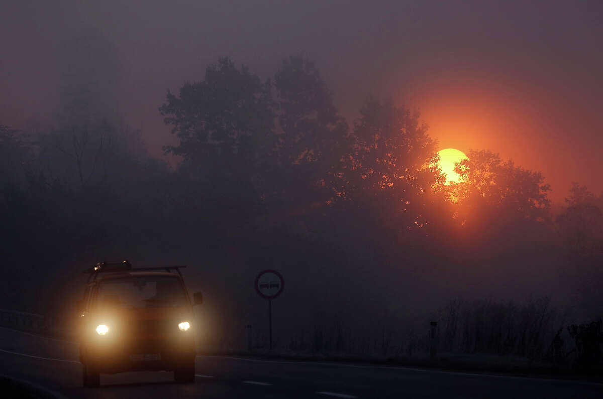 A passengers car drives along a foggy road as the sun rises near Sarajevo, Bosnia, Monday, Oct. 14, 2013. Morning fog is a regular occurrence in the Sarajevo valley, particularly during the cooler months of autumn.
