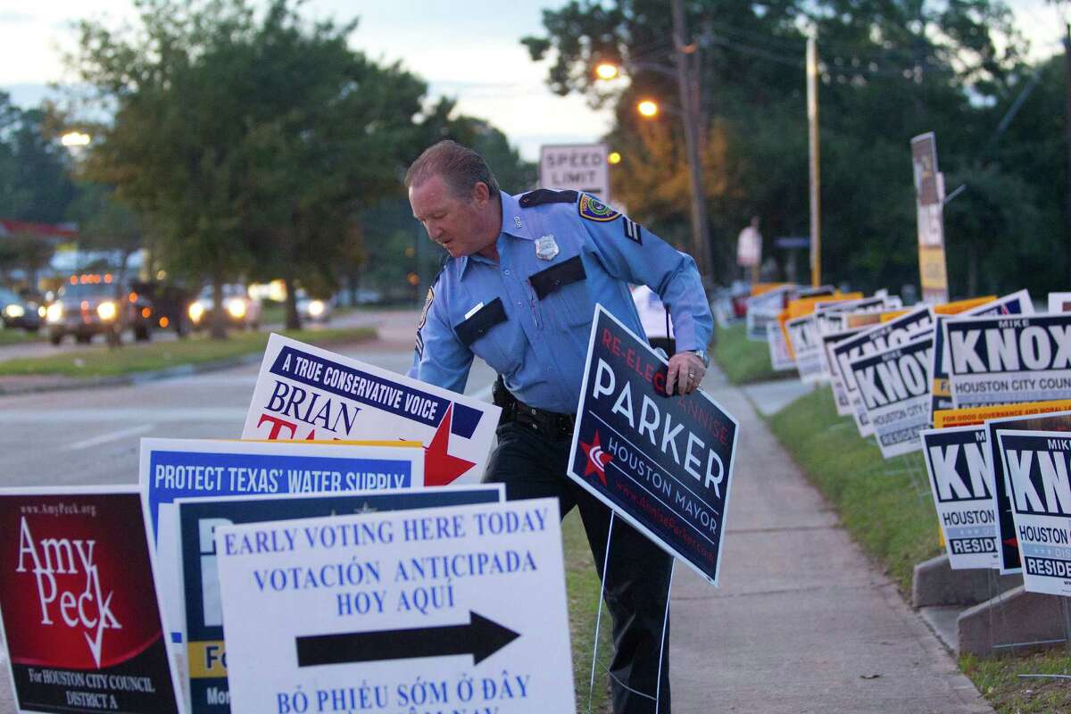 As early voting begins Monday, Houston police officer J.J. Mounsey removes campaign signs that are improperly placed between the sidewalk and street, causing a hazard for motorists, at a polling place in Spring Branch.