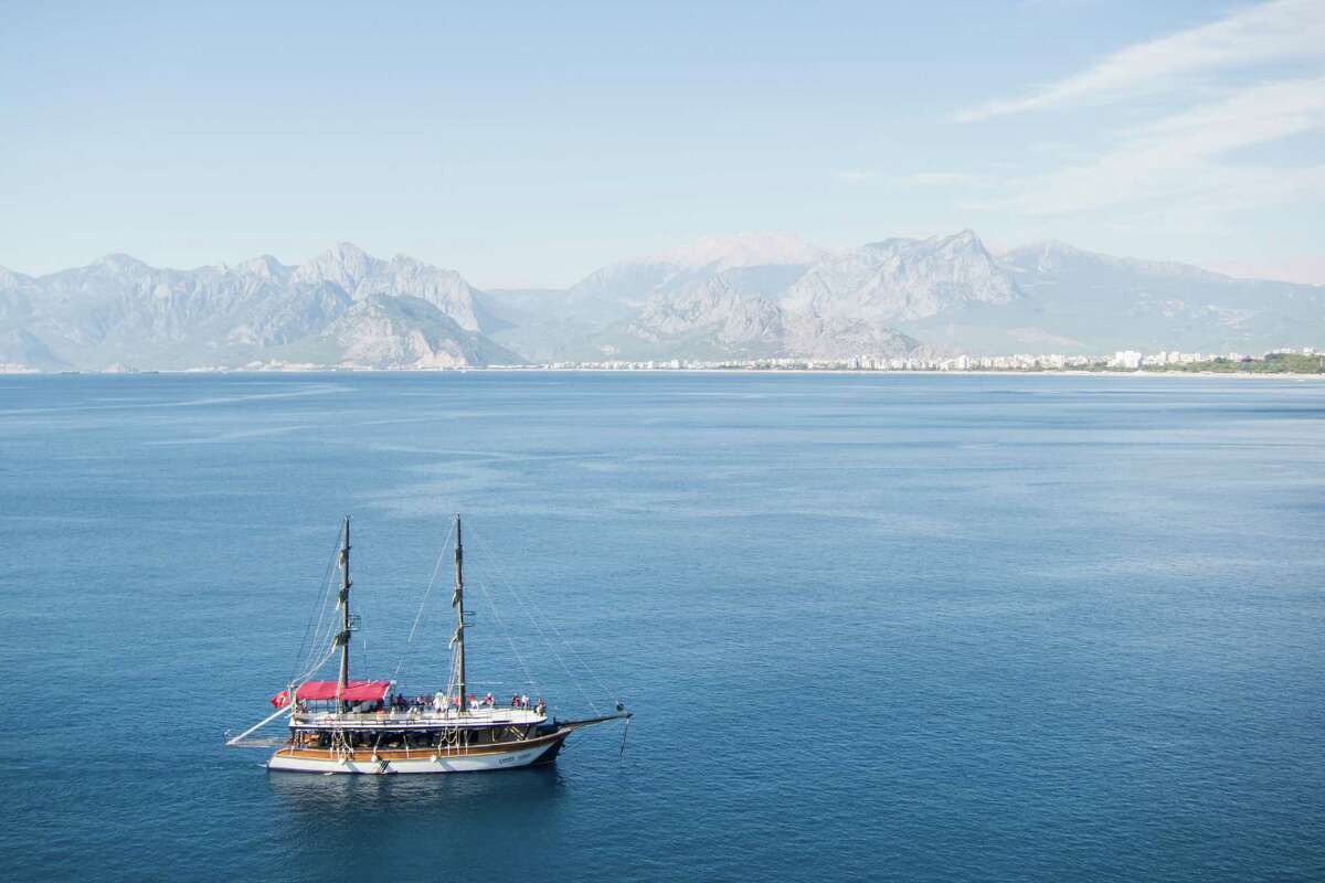 A sailboat cruises along the Mediterranean coastline in Antalya, Turkey.