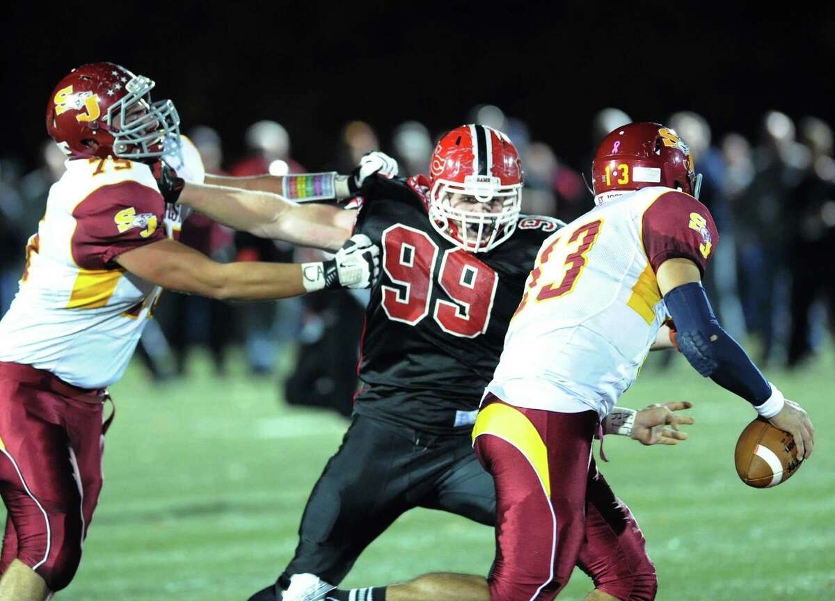 New Canaan's Connor Buck (# 99), at center, holds off St. Joseph blocker, Steve Hashemi (# 75), left, while chasing down St. Joseph quarterback Jordan Vazzano (# 13), right, during the high school football game between New Canaan and St. Joseph at New Canaan, Friday night, Nov. 1, 2013.