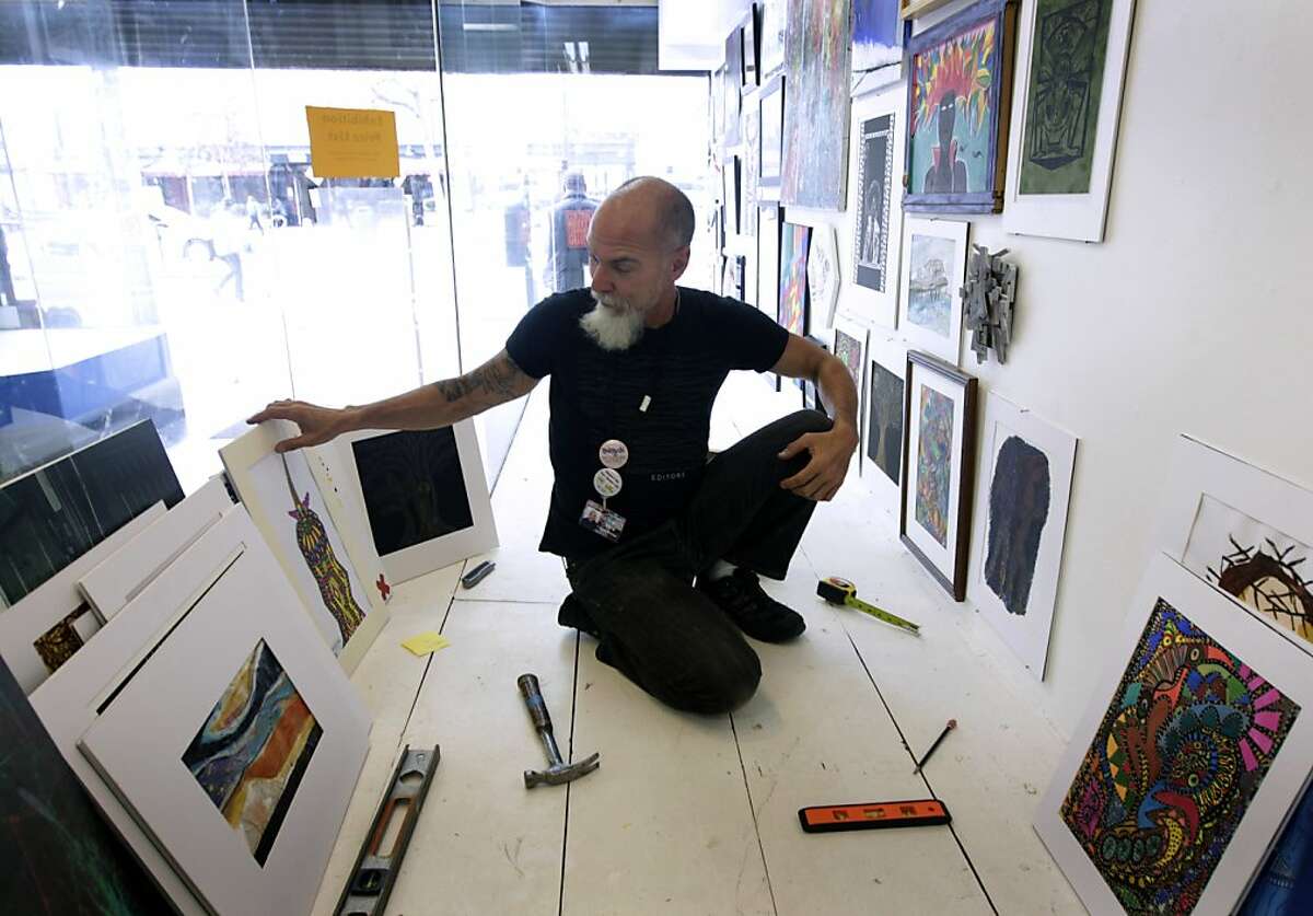 Ivan Vera, program manager at the Hospitality House Community Art Program, hangs artwork in the studio's storefront window in San Francisco, Calif. on Tuesday, Nov. 12, 2013. A nonprofit has stepped in to purchase the building and preserve the community arts programs in the mid-Market neighborhood.