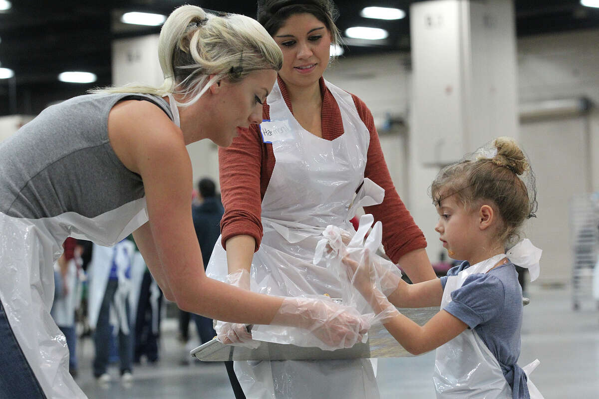 Celeste Jenkins, 5, right, gets help with glove from her mother, Ciara Ford, left, as they and Harmony Campbell prepare to serve slices of pumpkin pie at the Henry B. Gonzalez Convention Center during the 34th annual Raul Jimenez Thanksgiving Dinner, Thursday, Nov. 28, 2013.
