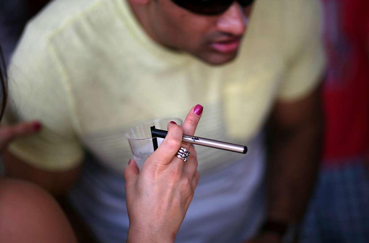 FILE -- Michele Dreiding smokes an e-cigarette while chatting with someone at a concert in New York, July 4, 2013. The city council weighing a law that would make New York the first major city in the country to ban the public use of e-cigarettes, which critics say is becoming increasingly common and sending a message to children that the devices are socially acceptable. (Yana Paskova/The New York Times)