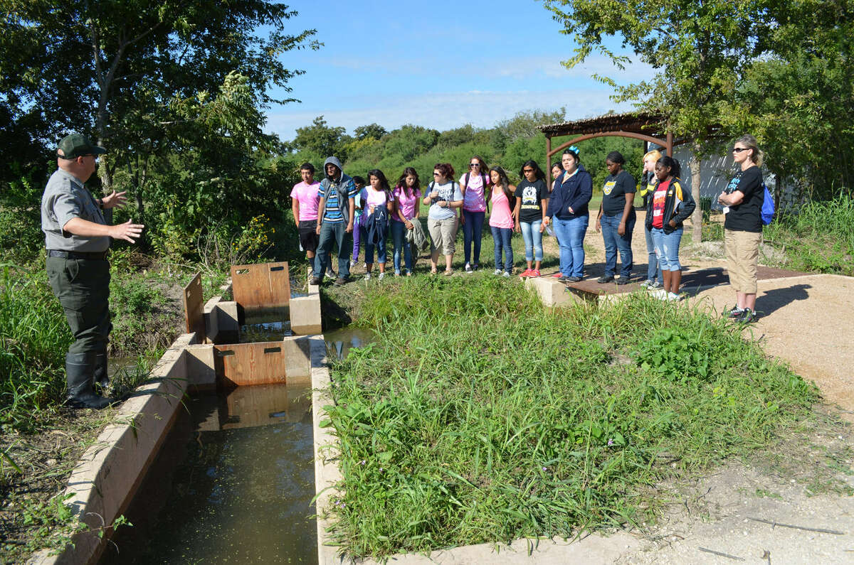 National Park Ranger Tom Castanos, left, explains to East Central High School students the workings of the acequia at the San Juan Demonstration Farm. By opening and closing gates, water can be diverted into fields that need irrigating.