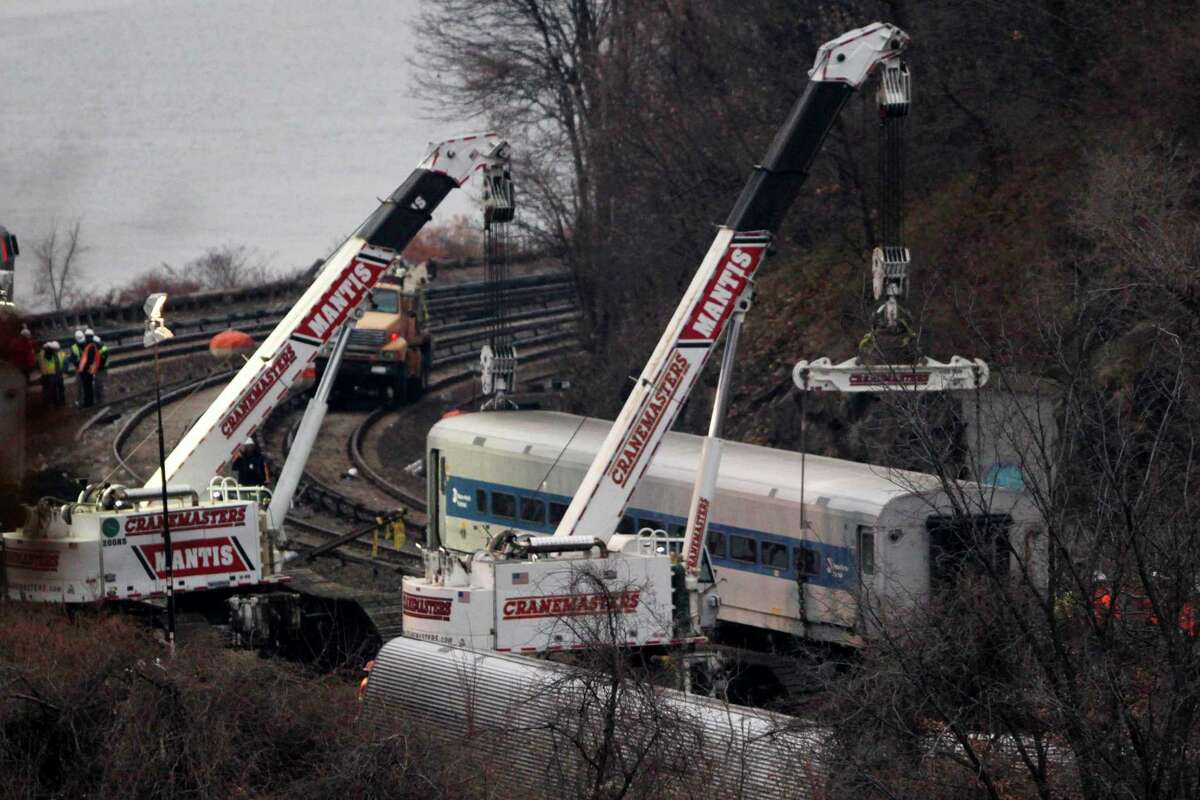 Cranes lift a derailed Metro-North train car, Monday, Dec. 2, 2013, in the Bronx borough of New York. Federal authorities began righting the cars Monday morning as they started an exhaustive investigation into what caused a New York City commuter train rounding a riverside curve to derail, killing four people and injuring more than 60 others. A second "event recorder" retrieved from the train may provide information on the speed of the train, how the brakes were applied, and the throttle setting, a member of the National Transportation Safety Board said Monday. (AP Photo/Mark Lennihan) ORG XMIT: NYML101