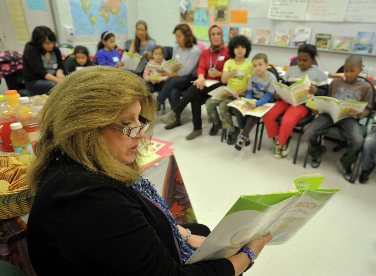Heidi Ganz, adult education ESL teacher, reads from the book "Trouble in the Barkers' Class" while the rest of the adult-oriented English as second language family literacy class follows along during the class' family day at Stark Elementary School in Stamford, Conn., on Thursday, Dec. 5, 2013. The class consists of people that speak six languages from 12 countries.