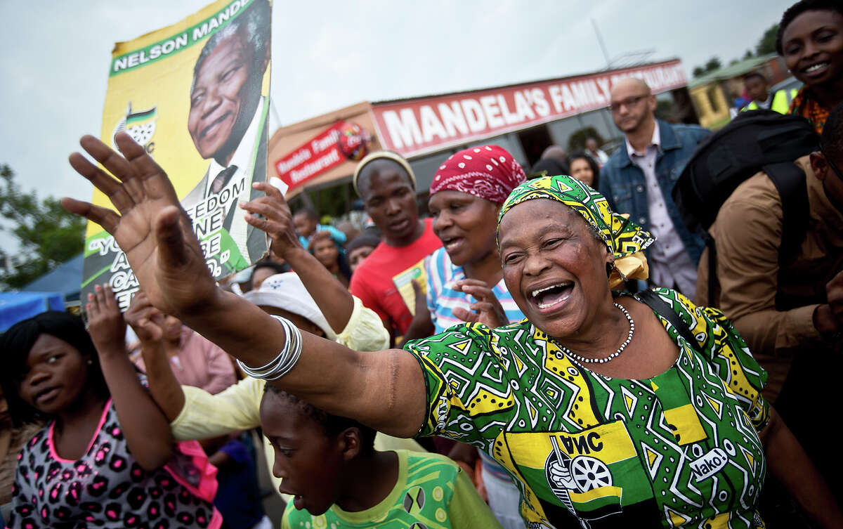 Mourners sing and dance to celebrate the life of Nelson Mandela, in the street outside his old house in Soweto, Johannesburg, South Africa, Friday, Dec. 6, 2013. Flags were lowered to half-staff and people in black townships, in upscale mostly white suburbs and in South Africa's vast rural grasslands commemorated Nelson Mandela with song, tears and prayers on Friday while pledging to adhere to the values of unity and democracy that he embodied.