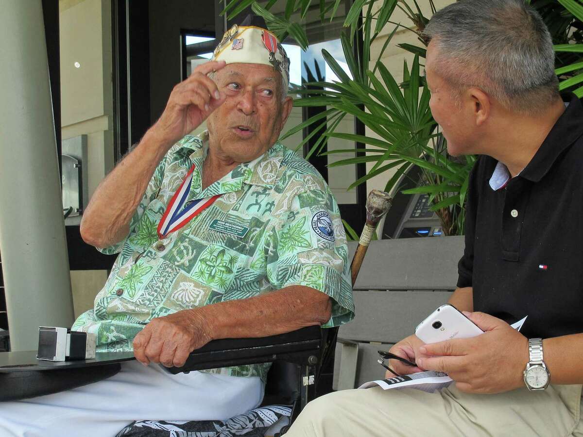 In this photo taken Nov. 22, 2013, Herb Weatherwax, left, talks to a visitor in Pearl Harbor, Hawaii. The 96-year-old retired electrician is one of four Pearl Harbor survivors who volunteers to greet people at the historic site. On Saturday is the 72nd anniversary of the 1941 attack by Japan on Pearl Harbor. (AP Photo/Audrey McAvoy)
