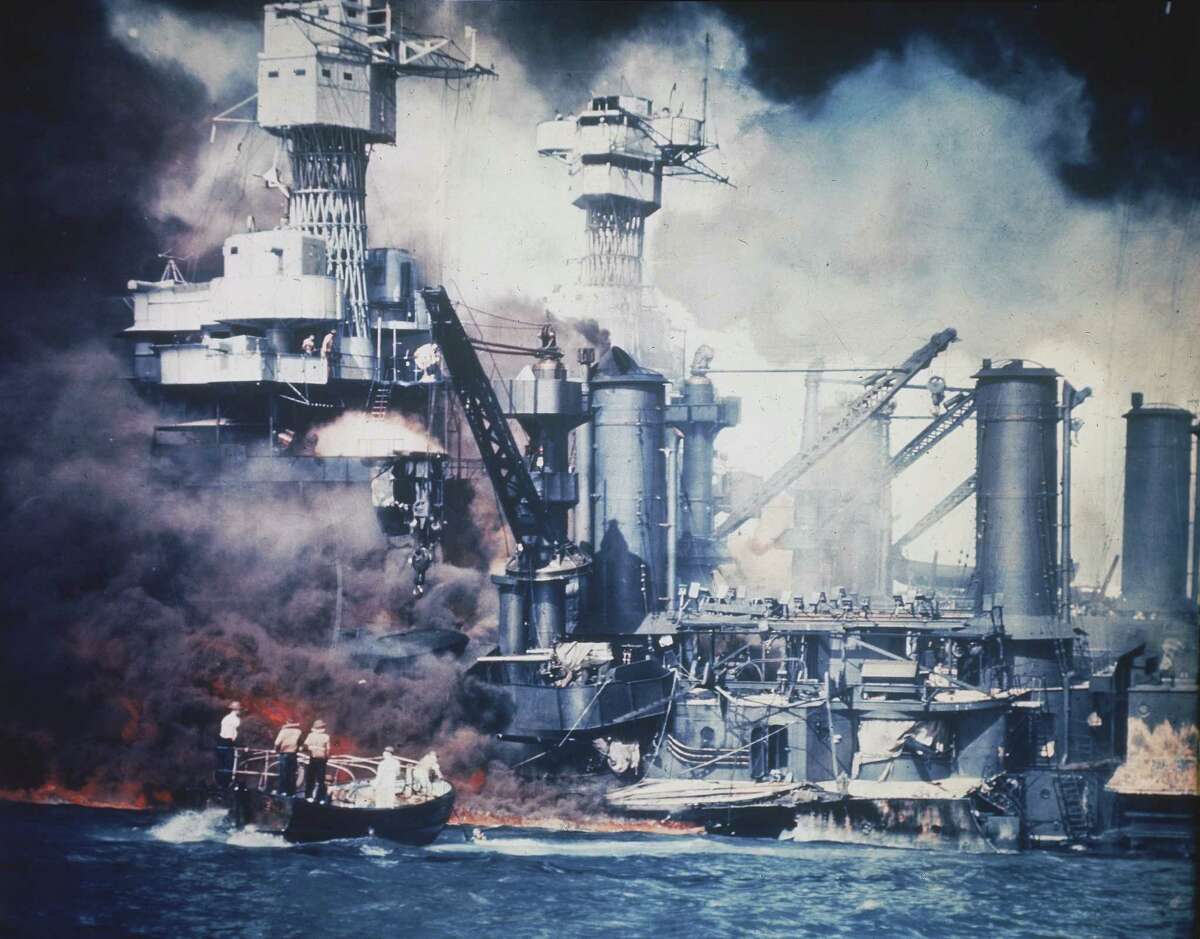 A small boat rescues a USS West Virginia crew member from the water after the Japanese bombing of Pearl Harbor, Hawaii on Dec. 7, 1941 during World War II. Two men can be seen on the superstructure, upper center. The mast of the USS Tennessee is beyond the burning West Virginia.
