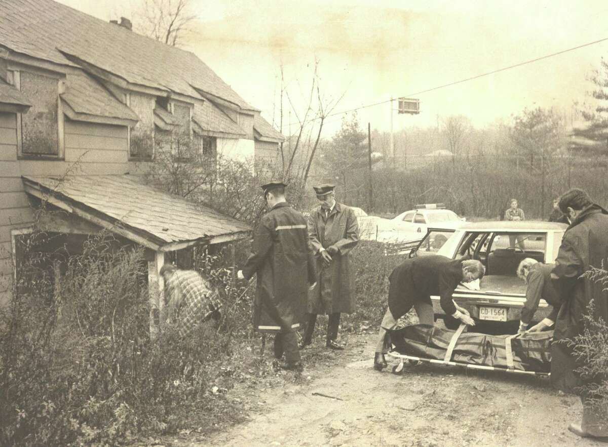 Darien Police search the grounds of the abandoned home where the body of Greg Sjolander was left. He was discovered on Monday, Dec. 4, 1978. To the left, police prepare to place Sjolander's body into the car.