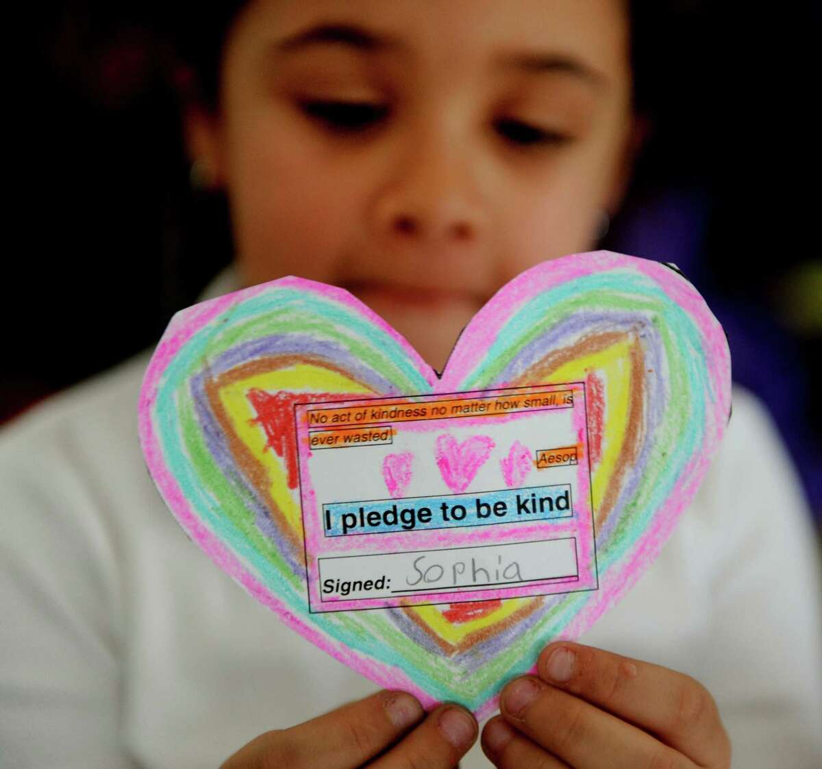 First grade student Sophia Servan holds up her pledge to be kind Thursday, Dec. 12, 2013 at Park City Magnet School. Staff and students at the school have each decorated and signed these hearts in memory of Sandy Hook victims.