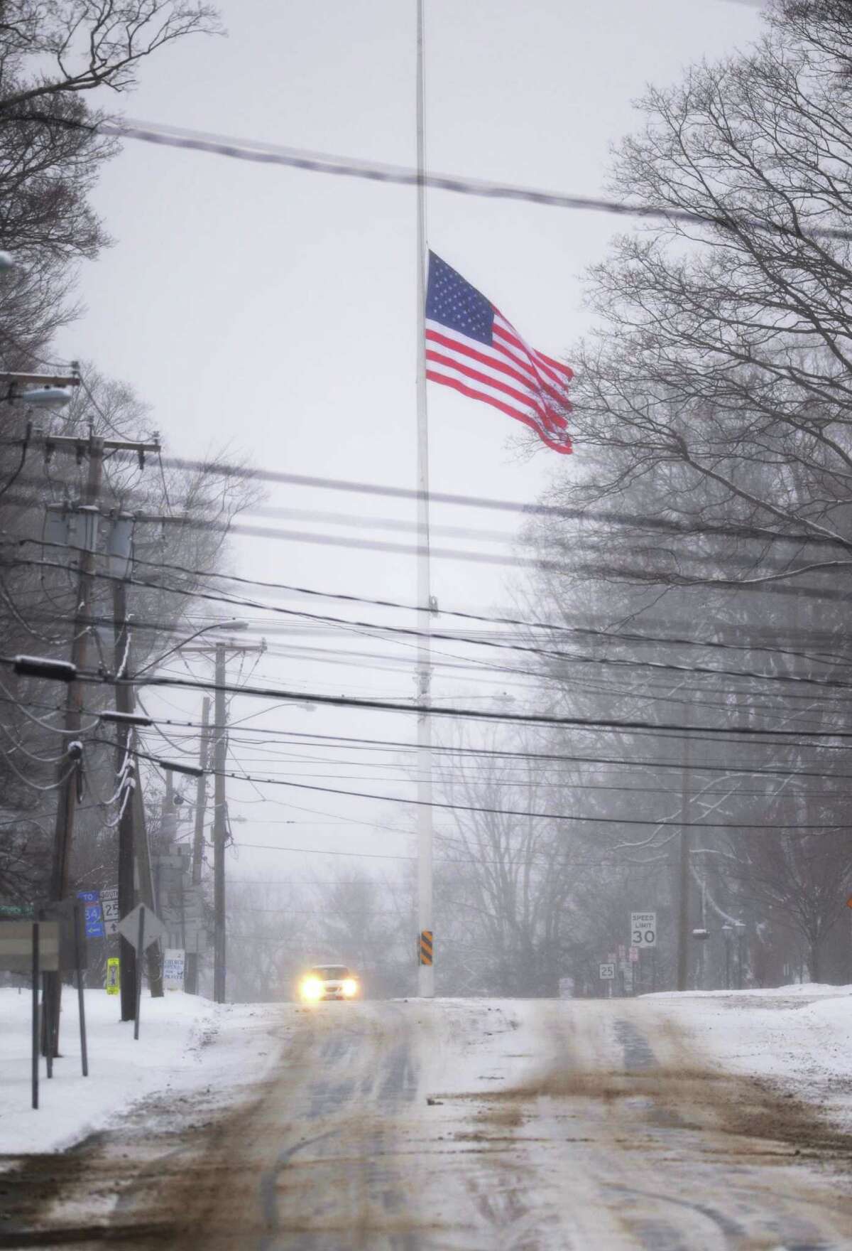 The flag at the intersection of Main Street and Church Hill Road in Newtown, Conn. is at half-staff on Saturday, Dec. 14, 2013, the one-year anniversary of the Sandy Hook Elementary School shooting that killed 26 students and educators. Snow fell on the town Saturday, casting a somber mood as residents remembered the tragedy one year ago.