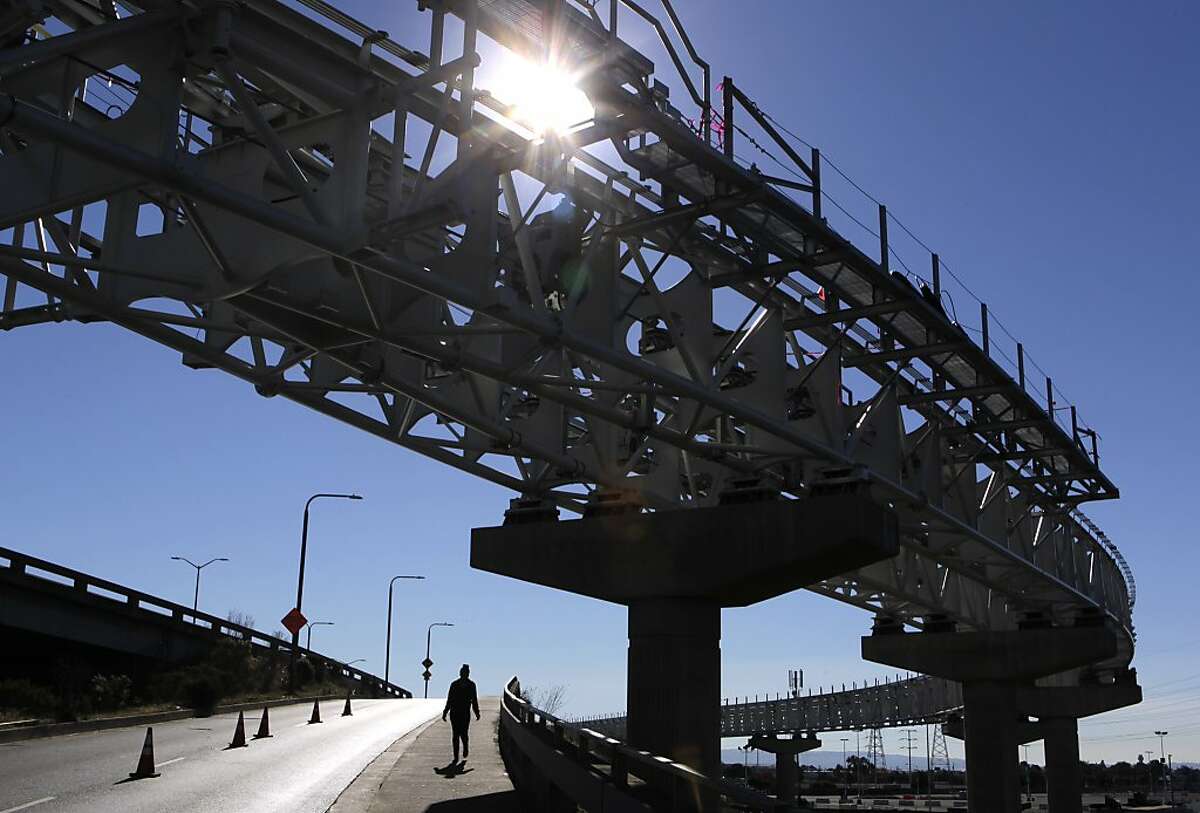 A woman walks on a ramp past elevated tracks of BART's Oakland Airport Connector in Oakland, Calif. on Friday, Dec. 20, 2013. When completed in late 2014, the 3.2 mile tram will provide a near seamless connection between the Coliseum BART station and Oakland International Airport.