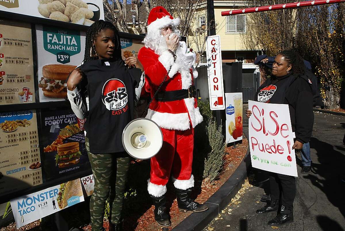 Rikia White (left) and Shonda Roberts (right), both employees at KFC, flank an unnamed Santa in front of the menu sign of the drive up window at the Jack in the Box at 6510 Telegraph Ave. in Oakland, Calif., on Friday, December 20, 2013. They protest in support of Ilda Amador, a pregnant fast food worker who was fired for speaking out at a demonstration.