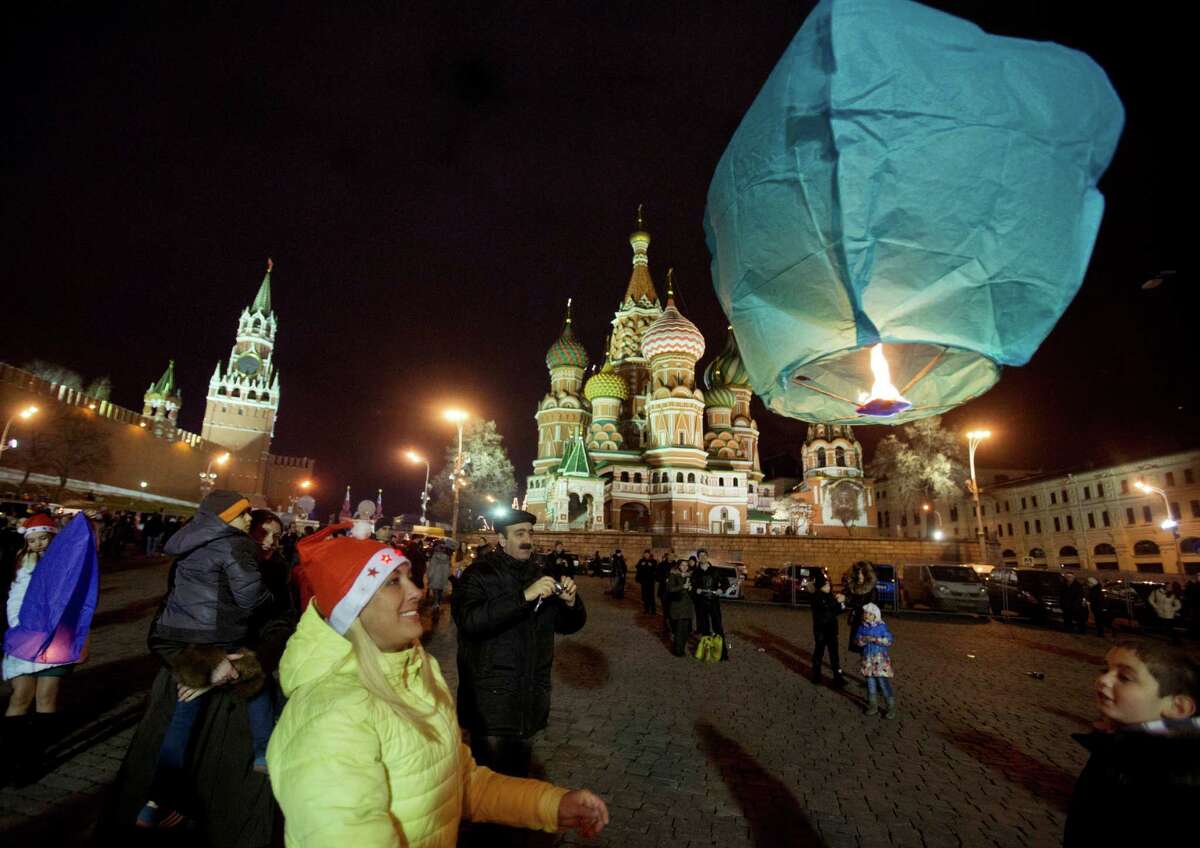 A woman launches a sky lantern during celebration for the New Year at the Red Square, in Moscow, Russia, early Wednesday, Jan. 1, 2014, with St. Basil Cathedral, centre right, and Kremlin's Spasskaya (Savior) Tower, left, are in the background. (AP Photo/Pavel Golovkin)
