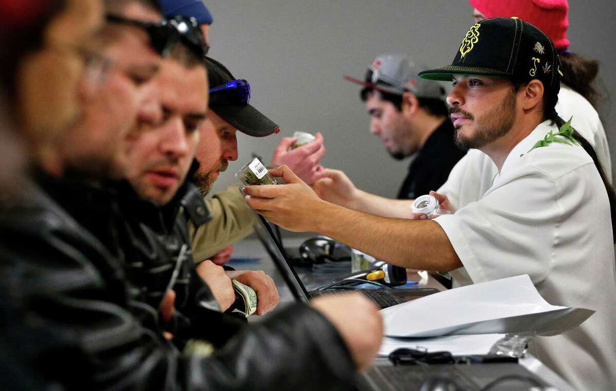 Employee David Marlow, right, helps a customer, who smells a strain of marijuana before buying it, at the crowded sales counter inside the Medicine Man retail store in Denver.