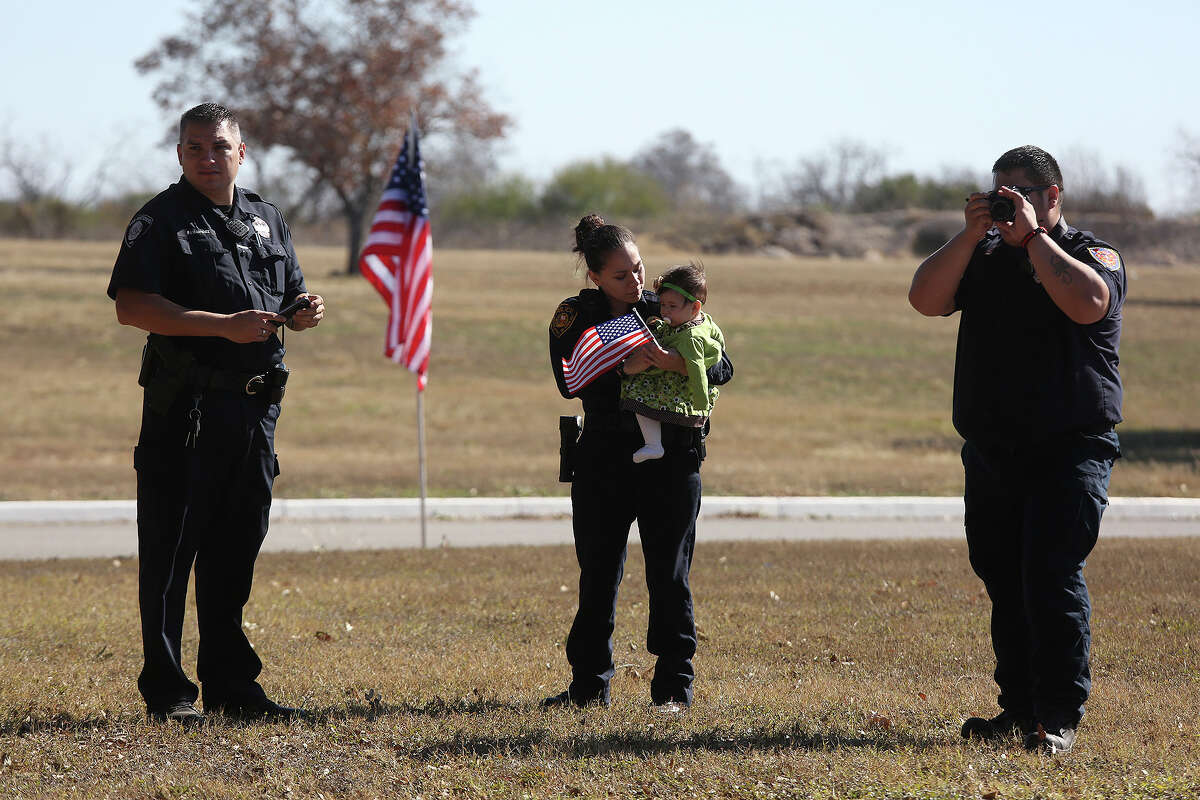 Sonny Perales, right, a paramedic with the City of Converse, right, stands with his wife, Savannah Perales, a police officer with South San ISD, holding their daughter, Sunny Perales, six months, and Charlie Benavidez, with San Antonio A2O, left, as he photographs the funeral procession for Officer Robert Deckard arriving at Mission Burial Park South in San Antonio on Saturday, January 4, 2014.