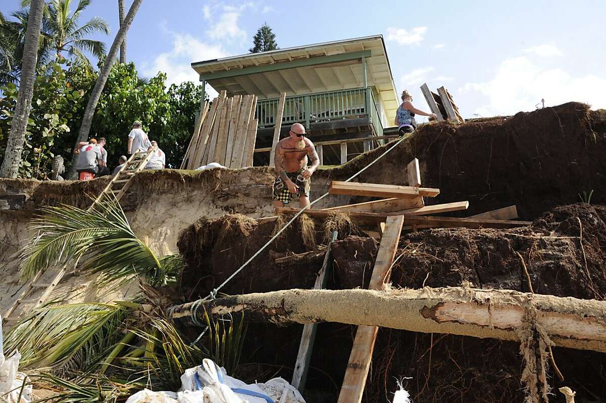 2014 JANUARY 2 CTY Ke Nui Road property owner Kenneth Dombrowski, at right, was cutting wood and bolstering his defenses against high waves. City and County of Honolulu Departments of Emergency Management, Facility Maintenance, and Parks and Recreation cleaning up debris on Sunset Beach. Erosion caused by a recent high surf episode that resulted in damage to several properties on Ke Nui Road near Rocky Point. SA photos by Craig T. Kojima