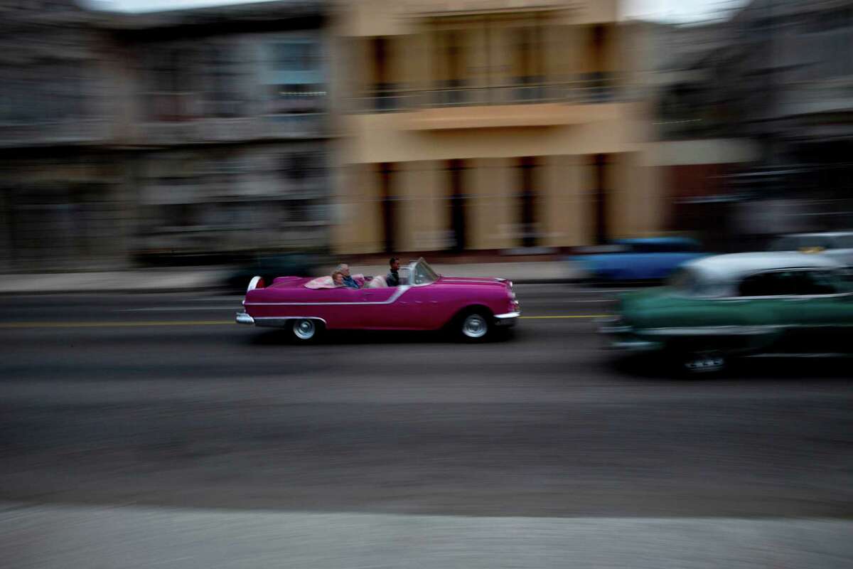 Tourists ride in a classic American car that serves as a taxi in Havana, Cuba, Thursday, Dec. 19, 2013. In many parts of Havana, the cityscape is changing rapidly. Along once darkened streets, pedestrians now walk through the neon glow of signs advertising new bars, restaurants and rooms for rent. Increasingly, late-mode European and Asian automobiles share the road with vintage Chevrolets and boxy Russian Ladas, idling at new stoplights. (AP Photo/Ramon Espinosa)