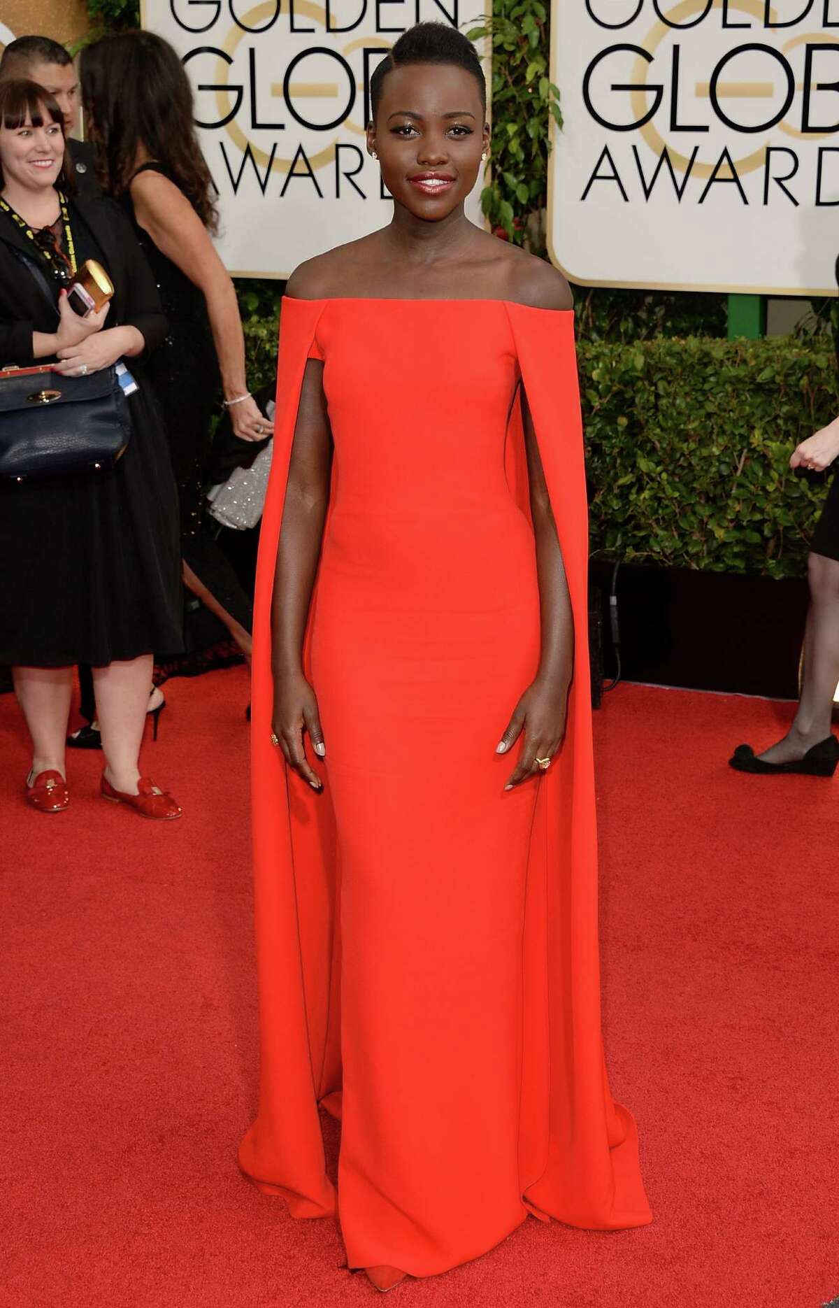 Lupita Nyong'o is a caped wonder in her orange-red Ralph Lauren gown with minimal accessories. This is how to do it.