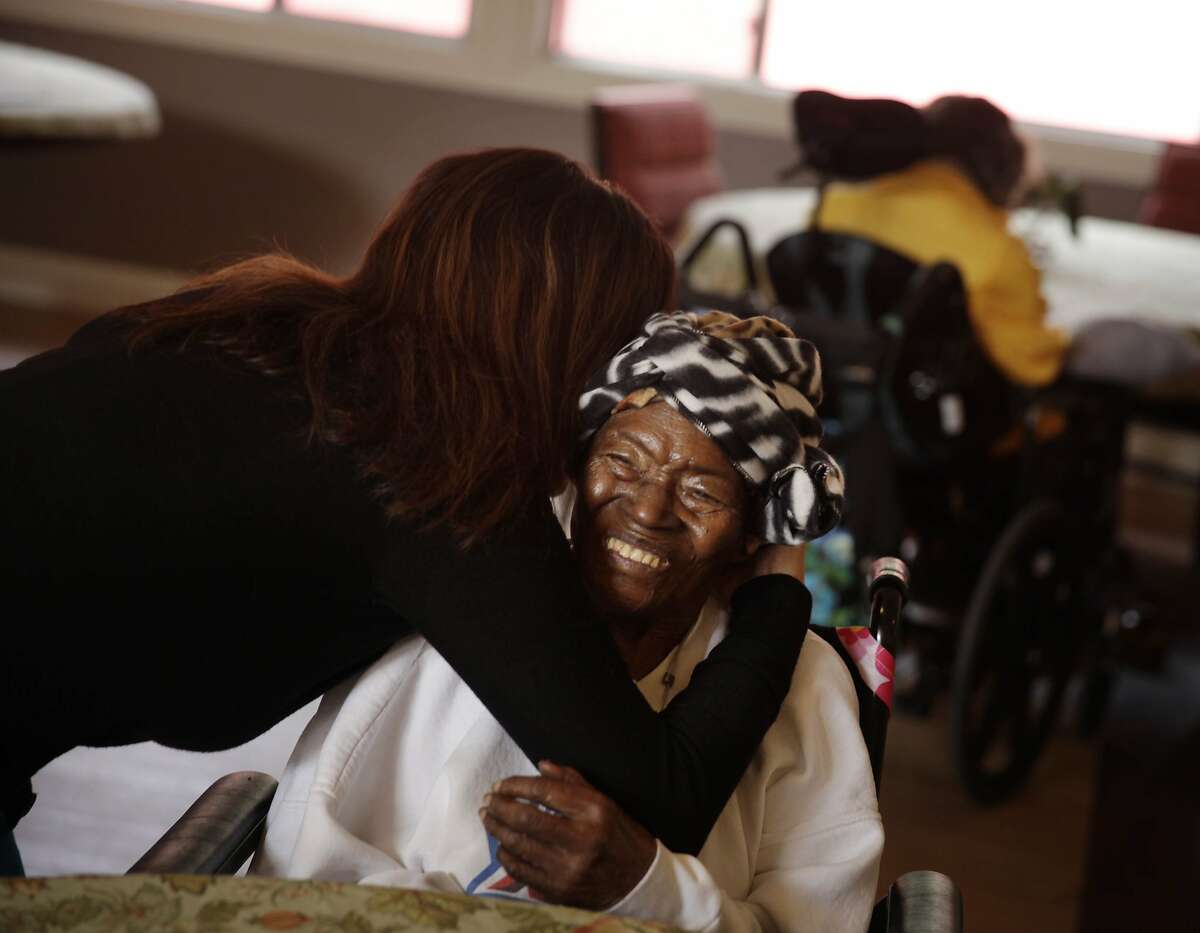 Cristina Flores (l to r), Agesong chief operating and program officer, gives Velma Shaw a hug in a dining area at WoodPark on Monday, November 18, 2013 in Oakland, Calif.