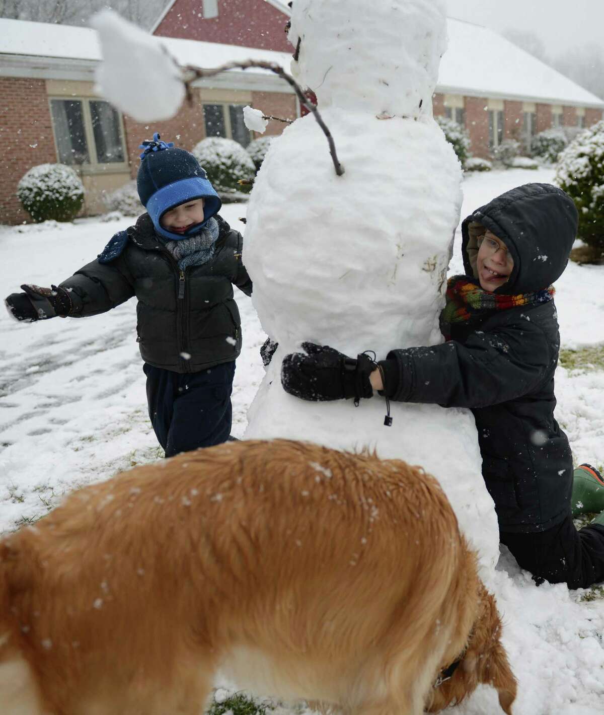 Isaiah Morris, left, 4, and his brother Elijah, 7, hug a snowman that they built in front of Christ the King Lutheran Church in Newtown, Conn. on Saturday, Jan. 18, 2014. The area received a surprise snowstorm Saturday, with Danbury getting just one inch of snow but other areas getting up to three inches.