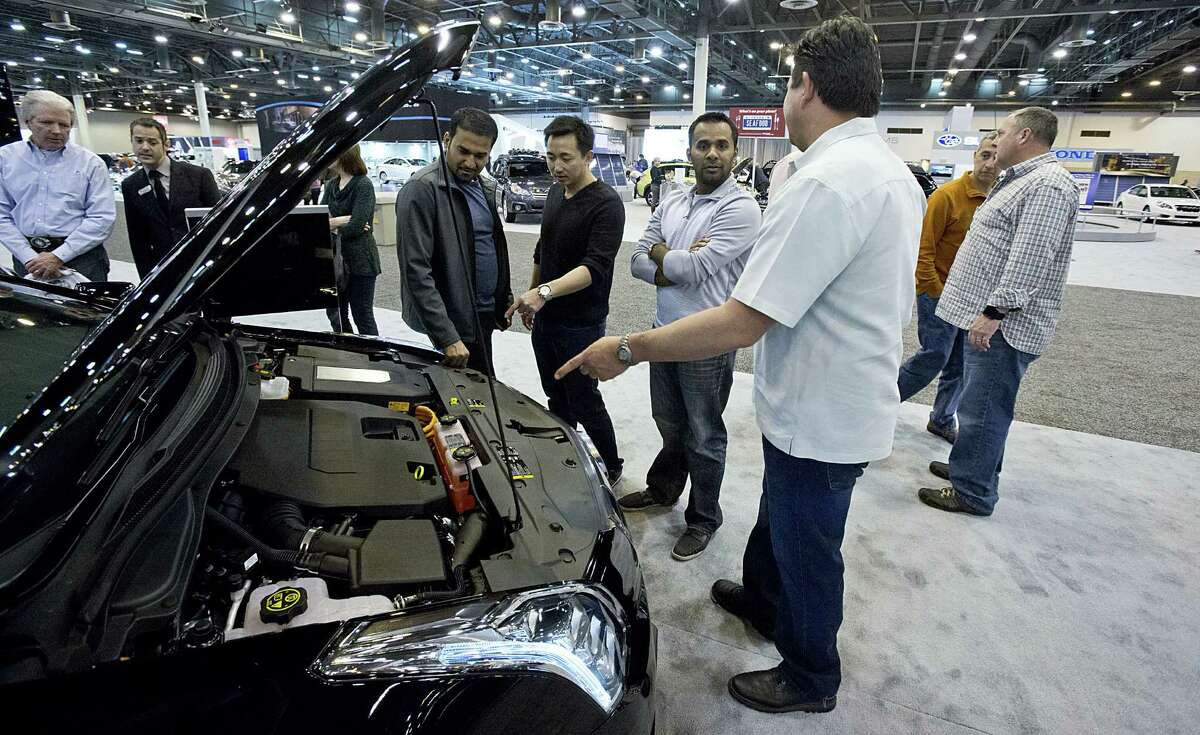 Hung Dang (wearing black, pointing) and friends look at the engine of the fully electric Cadillac ELR at the Houston Auto Show. The ELR can go 37 miles before dipping into gasoline reserves.