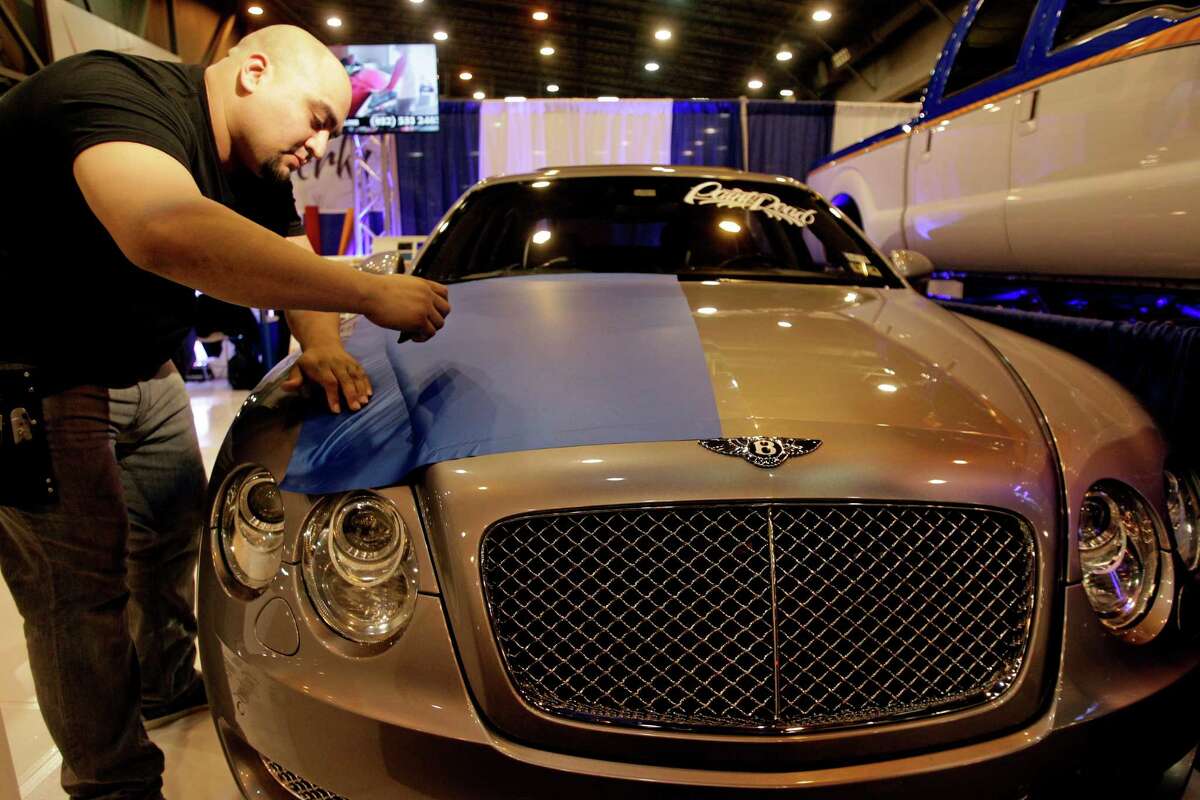 Gabe Garcia, co-owner of Vinyl Werkz Customs, shows how to apply a blue wrap to the hood of a Bentley at the auto show.